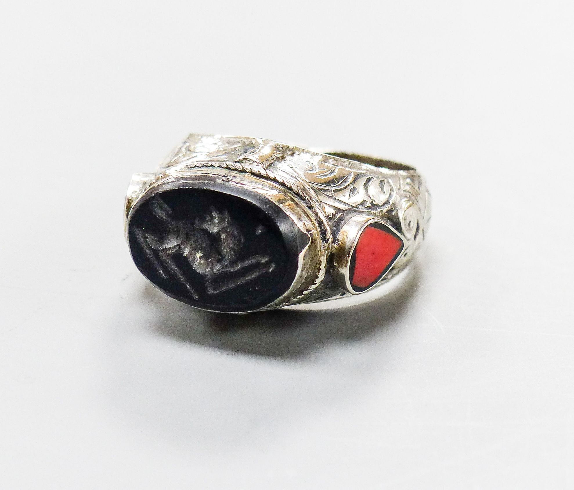 A continental engraved white metal and oval intaglio black onyx ring, with two colour enamel set shoulders, size S/T, gross weight 18.8 grams.